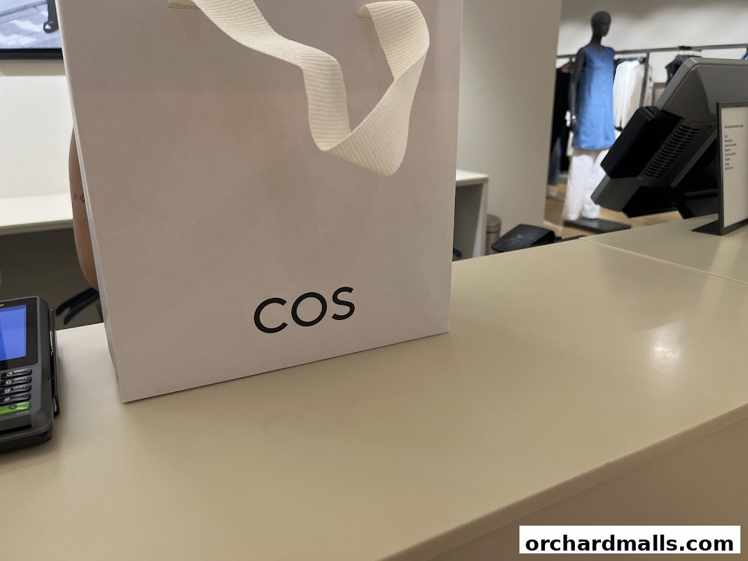 A white shopping bag with the COS logo sits on a counter in a clothing store.