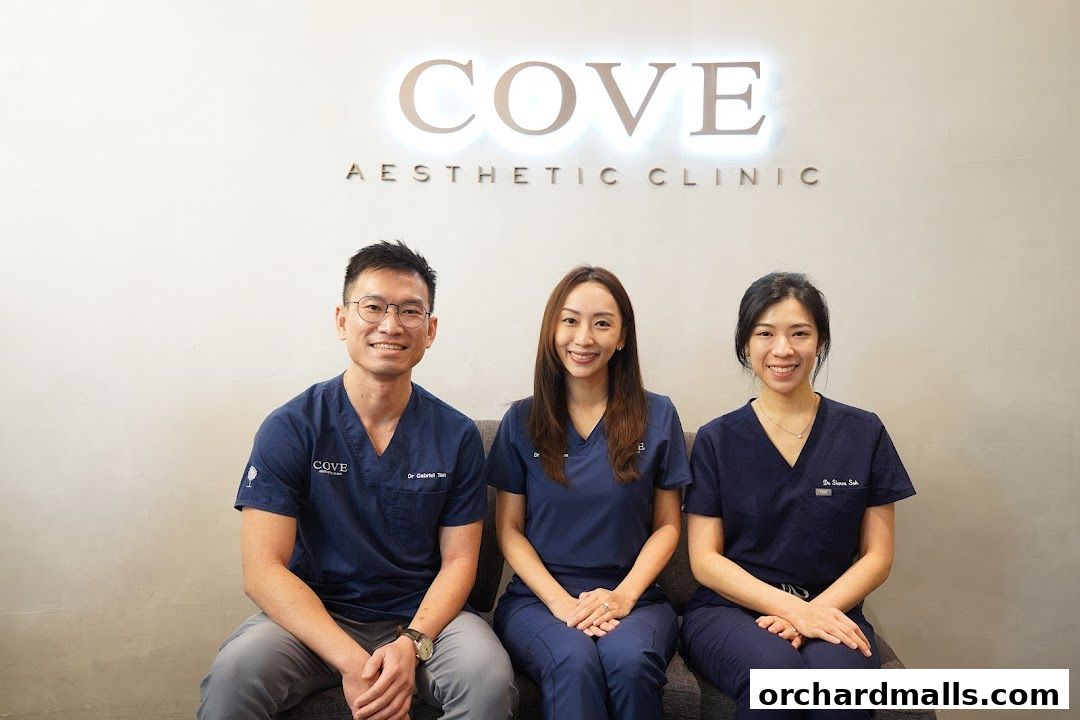 Three medical professionals smiling in navy blue scrubs in front of a clinic sign.