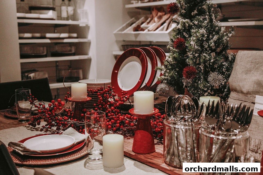 A festive table setting with red berries, candles, plates, and cutlery, alongside a small Christmas tree.