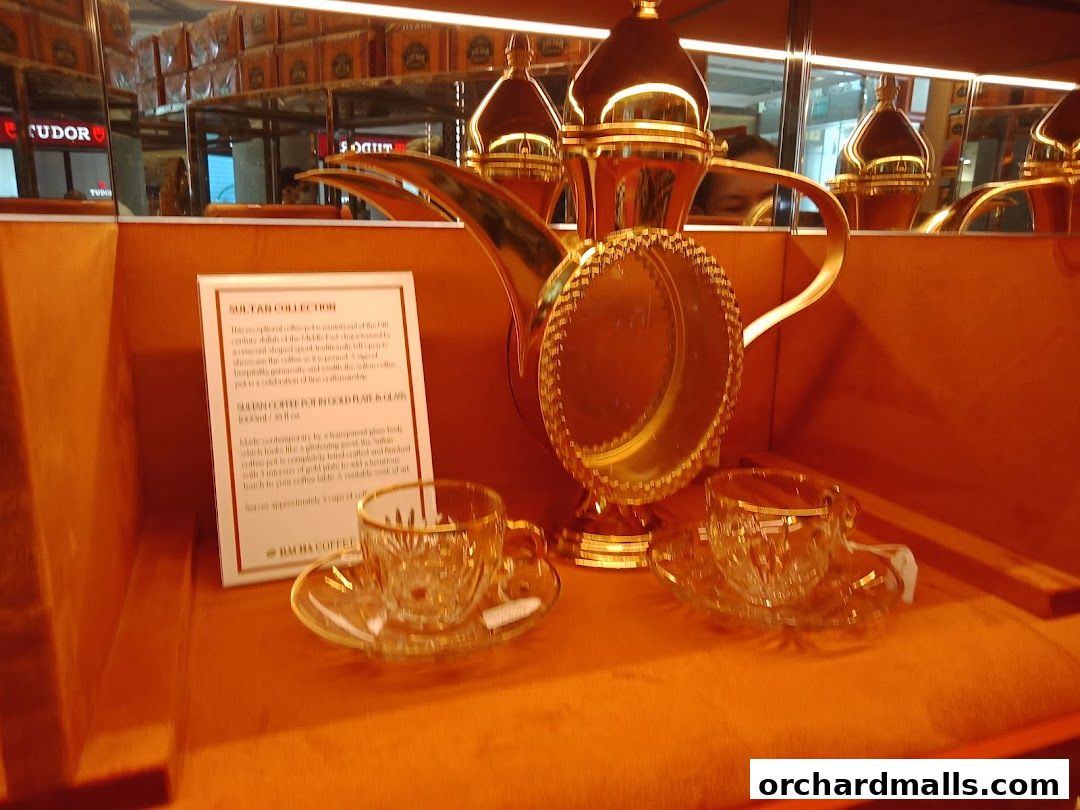 A golden coffee pot and two crystal cups and saucers are displayed.