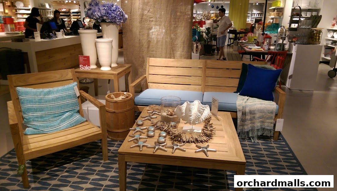 Crate and Barrel store interior featuring a wooden outdoor furniture set with blue cushions and decorative items.