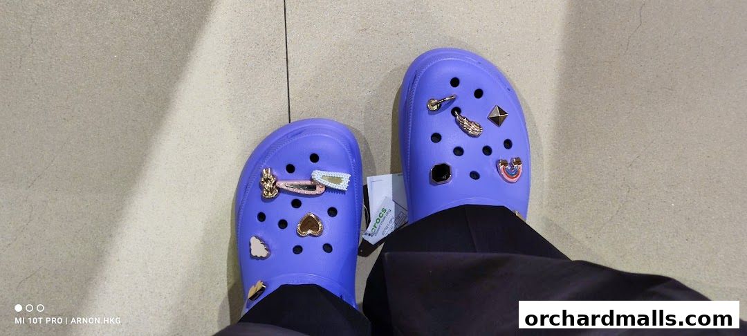 A pair of purple Crocs adorned with various charms, including a rainbow and a heart.