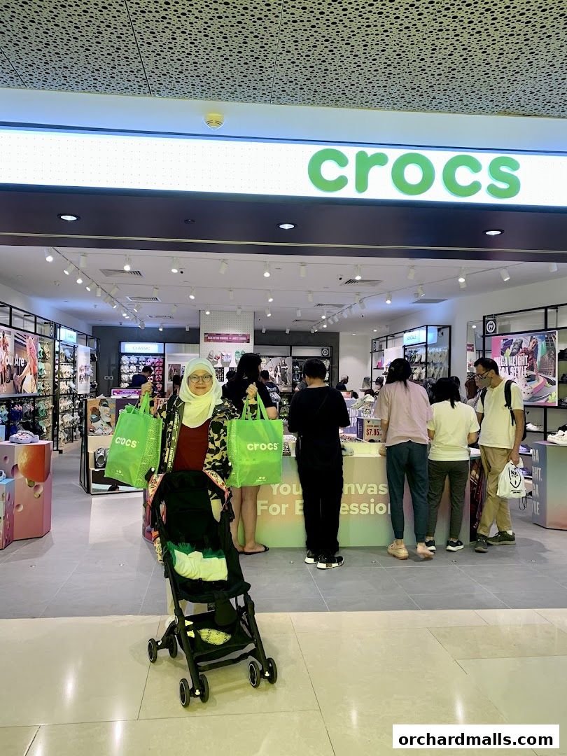 People are shopping at a Crocs store, with a woman holding shopping bags and a stroller.
