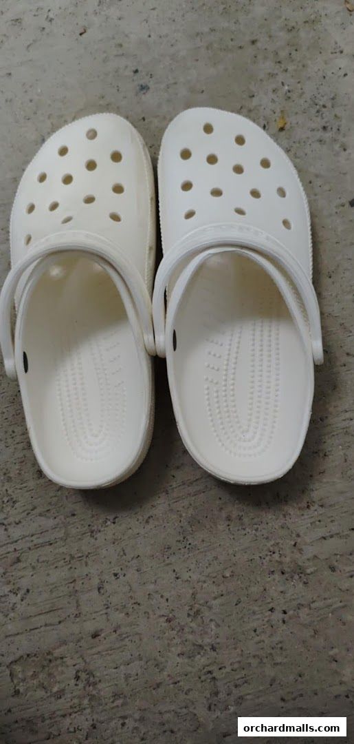A pair of white Crocs clogs are displayed on a textured concrete surface.