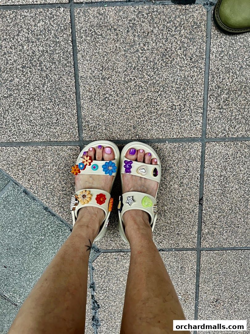 A person's feet wearing white Crocs sandals decorated with colorful Jibbitz charms.