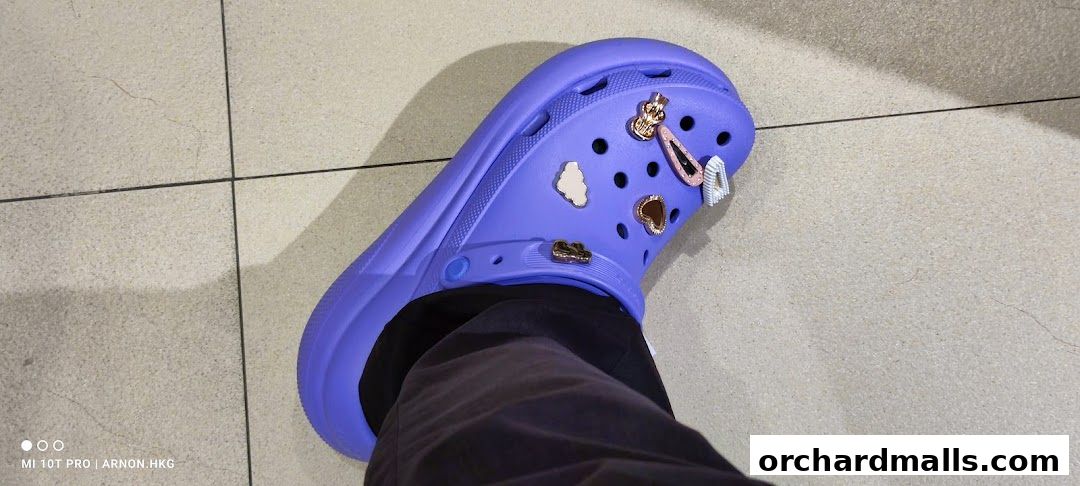 A close-up of a purple Croc shoe adorned with various charms, including a crown and a heart.