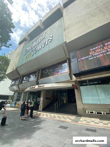 The entrance of Orchard Towers building with people walking on the sidewalk.