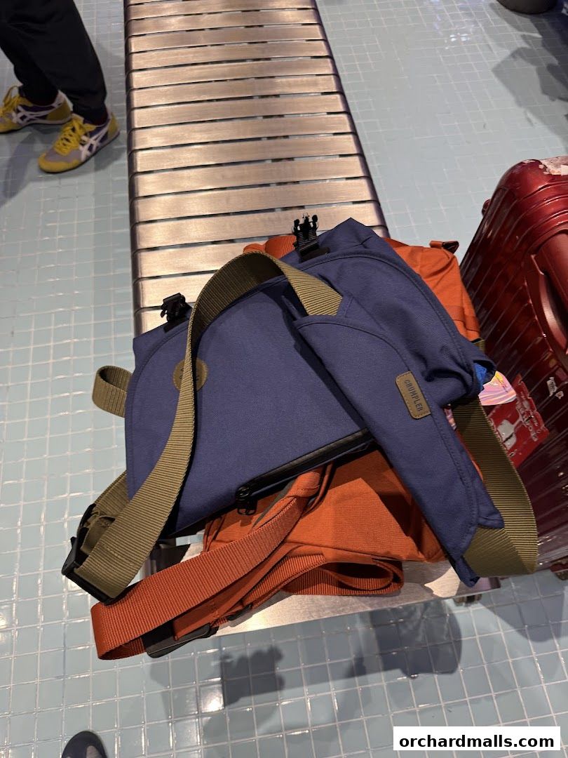 A collection of bags, including a blue Crumpler bag, on a metal bench with a red suitcase nearby.