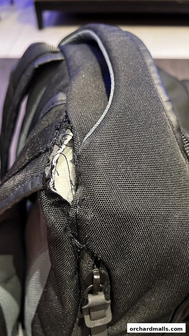 Close-up of a black backpack strap showing wear and tear with visible stitching.