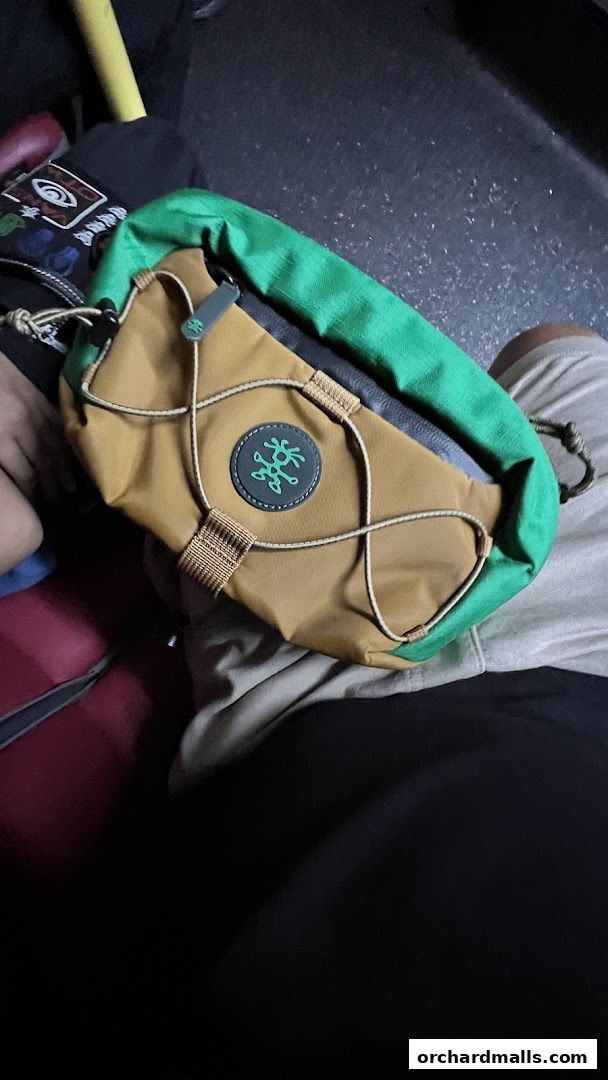 A close-up shot of a tan and green Crumpler fanny pack with a distinctive logo.
