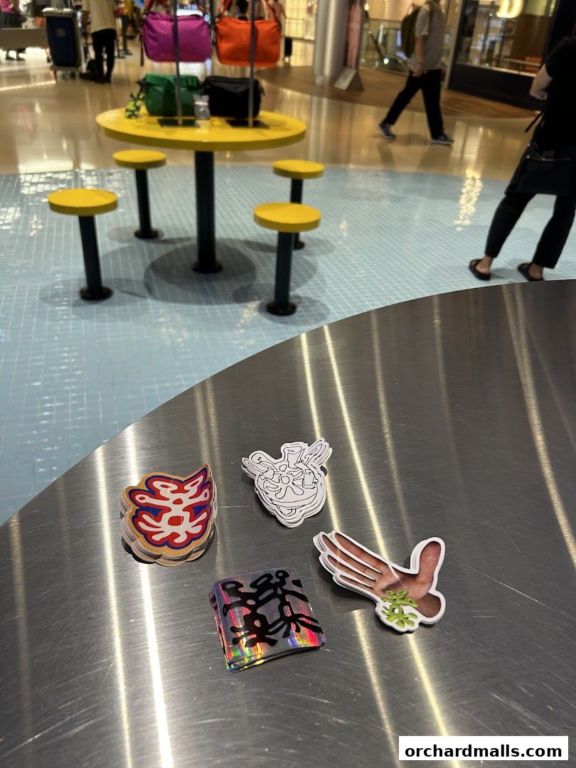 Stickers are displayed on a metallic table in front of a yellow table and chairs.