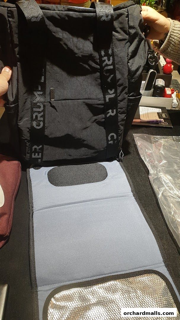 A black Crumpler bag with branded straps is shown, partially unfolded with a padded mat.