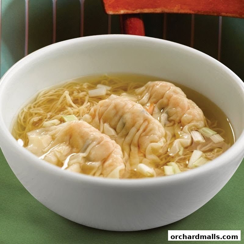 A bowl of wonton noodle soup with three wontons and chopped scallions.