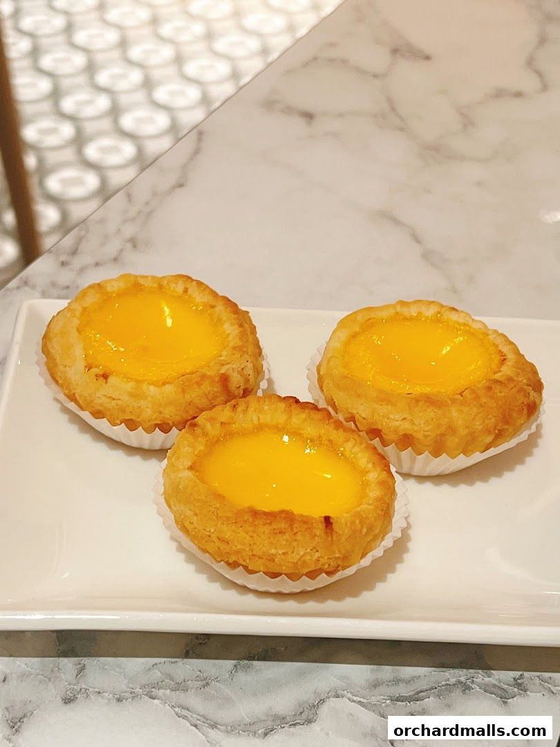 Three golden egg tarts on a white plate, ready to be enjoyed.