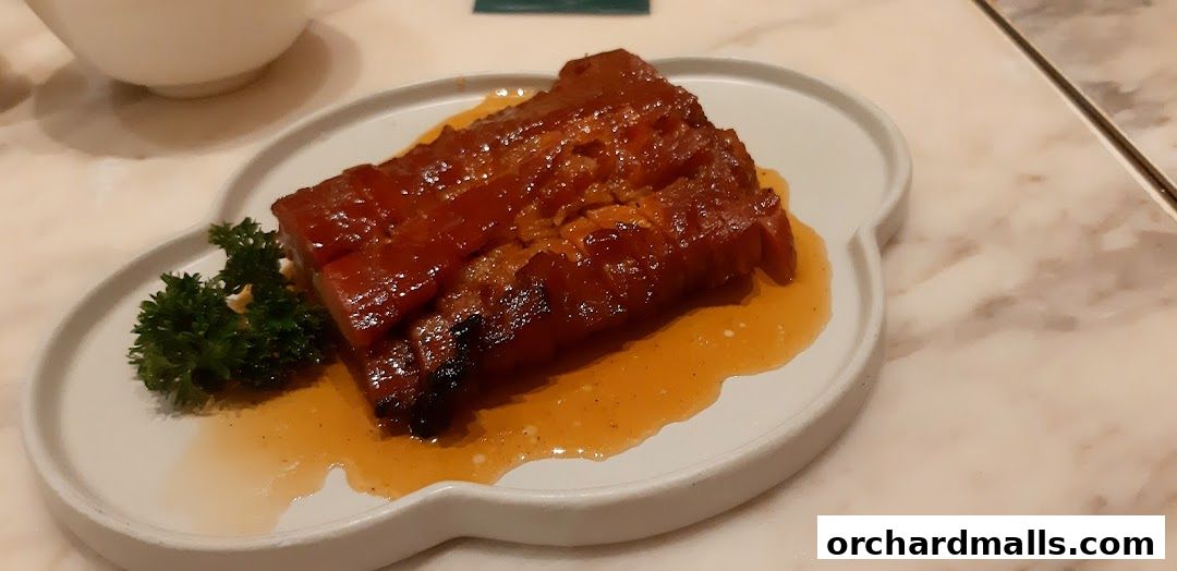 A close-up of a glazed meat dish with a sprig of parsley on a white plate.