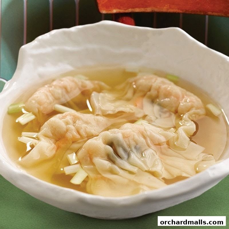 A close-up of a bowl of wonton soup with chopped scallions.