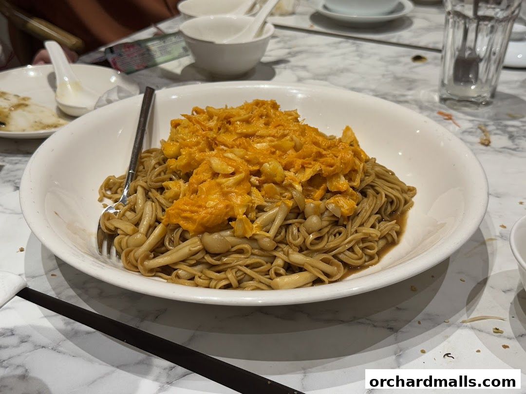 A bowl of noodles with mushrooms and a bright orange topping, served at a restaurant.