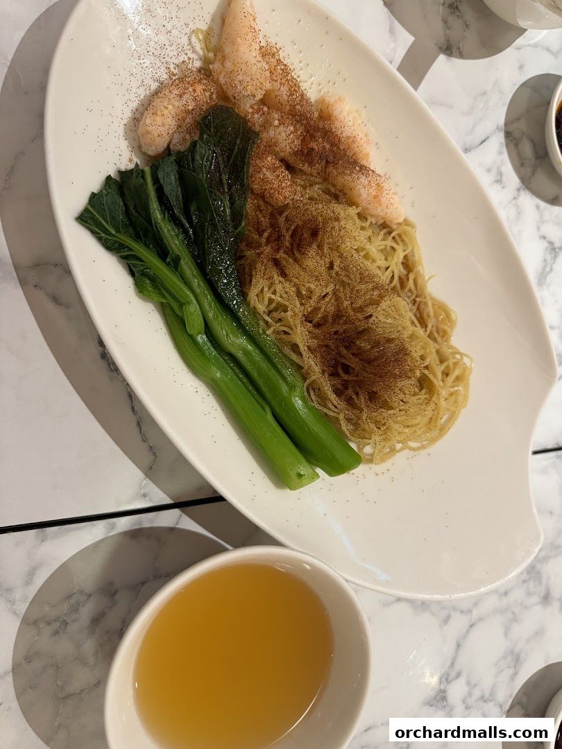 A plate of noodles with shrimp and greens, served with a side of broth.
