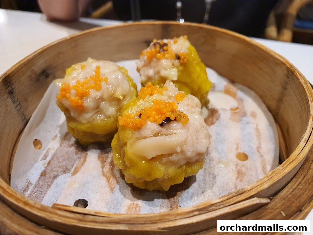 Three delicious dim sum dumplings topped with orange roe in a bamboo steamer.