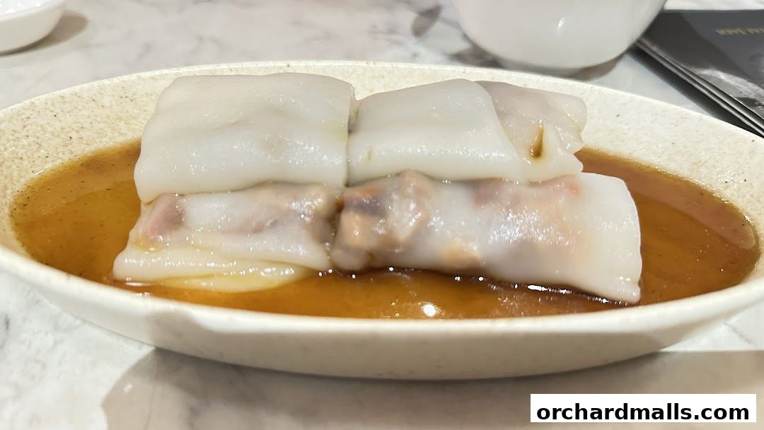 A close-up of steamed rice noodle rolls filled with meat in a savory sauce.