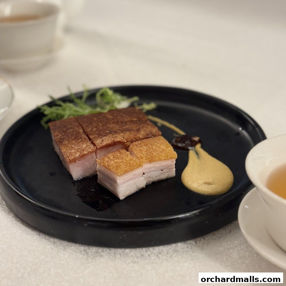 Crispy roasted pork belly served with a side of mustard sauce and garnish.