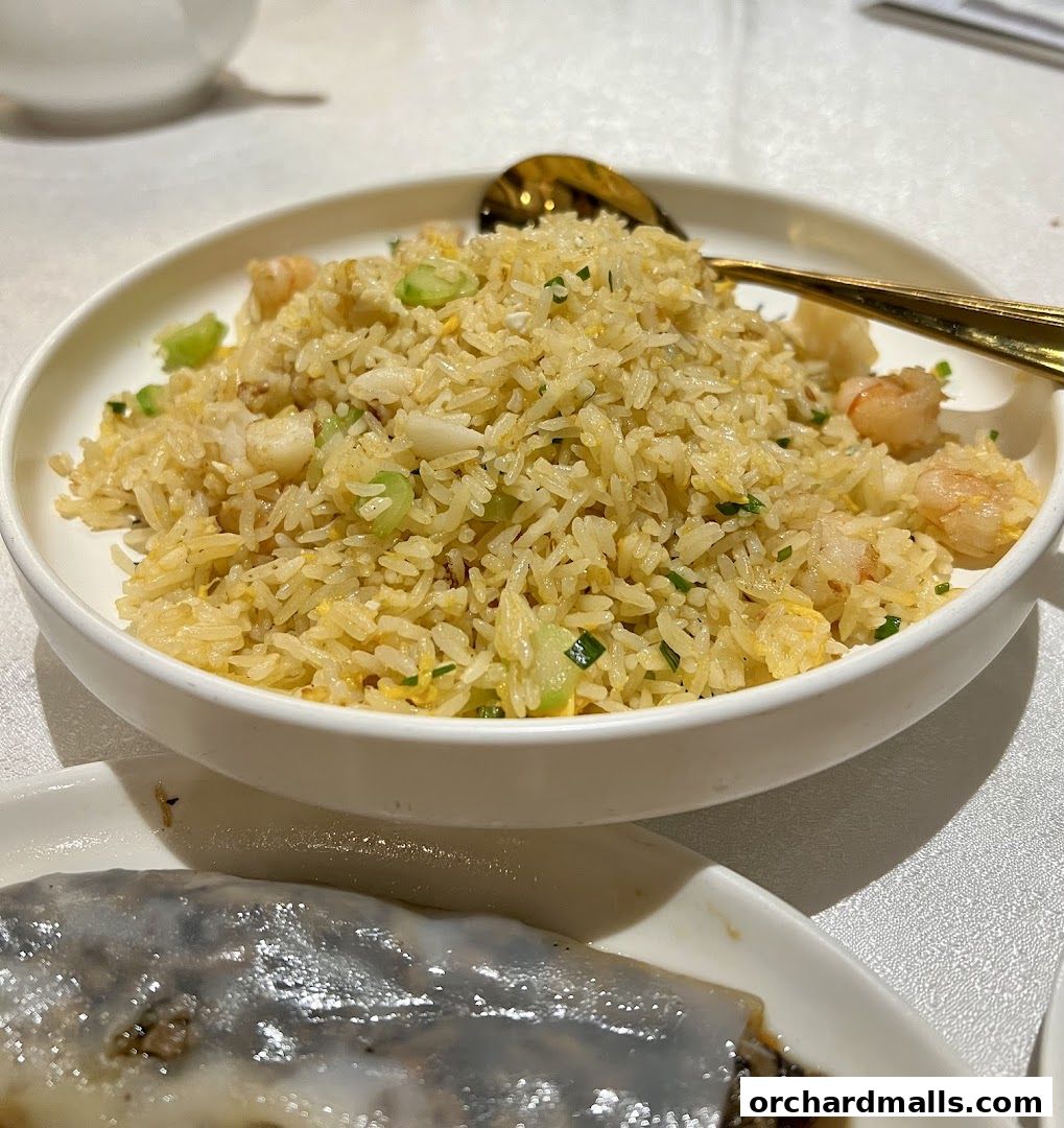 A close-up of a bowl of fried rice with shrimp and vegetables, served with a golden spoon.