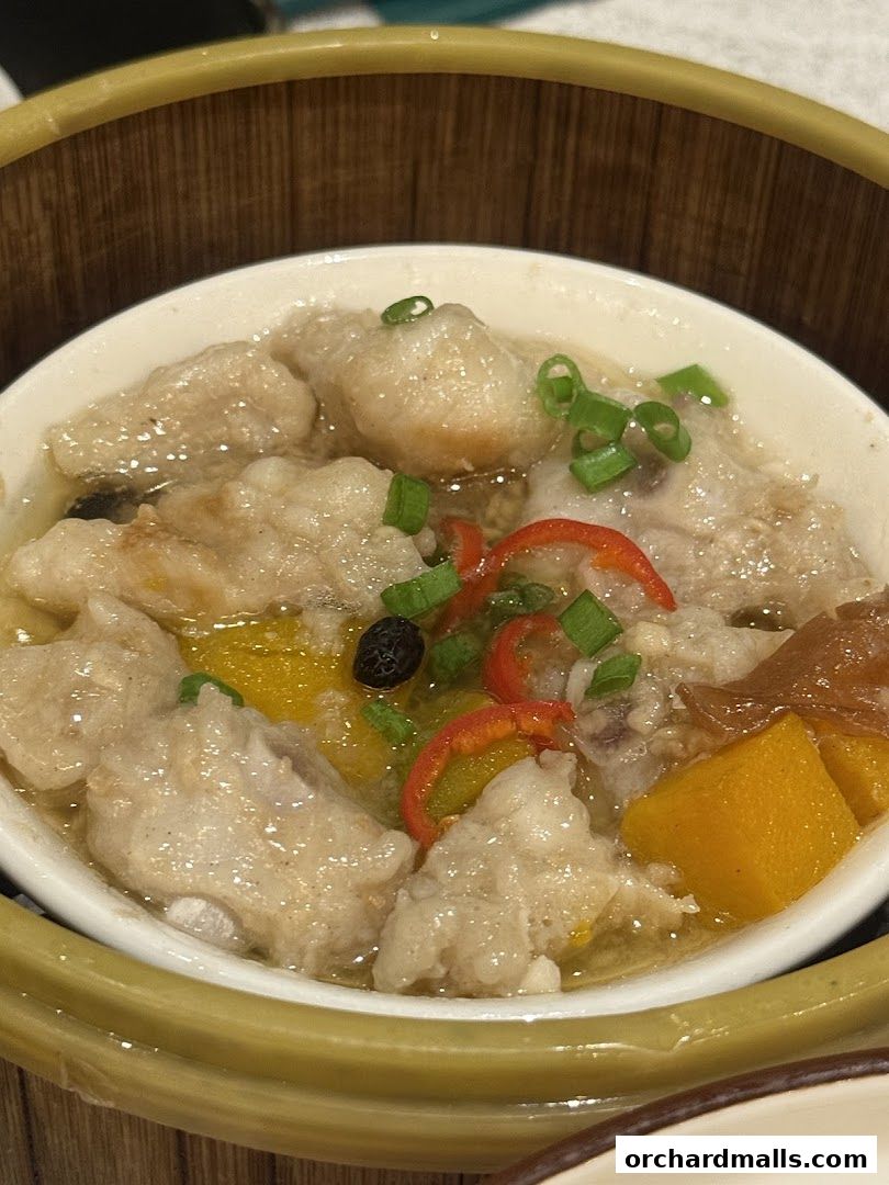 A close-up of a steamed dish with fish, pumpkin, and chili in a bamboo steamer.