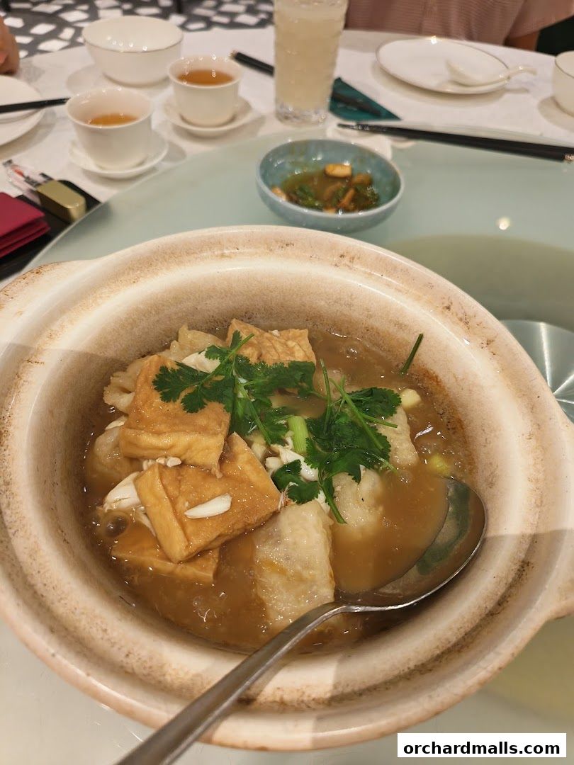 A close-up of a clay pot dish with tofu, seafood, and herbs, served with tea.