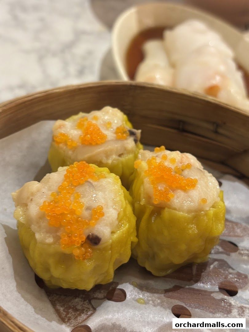 Close-up of three delicious dim sum dumplings topped with orange roe in a bamboo steamer.