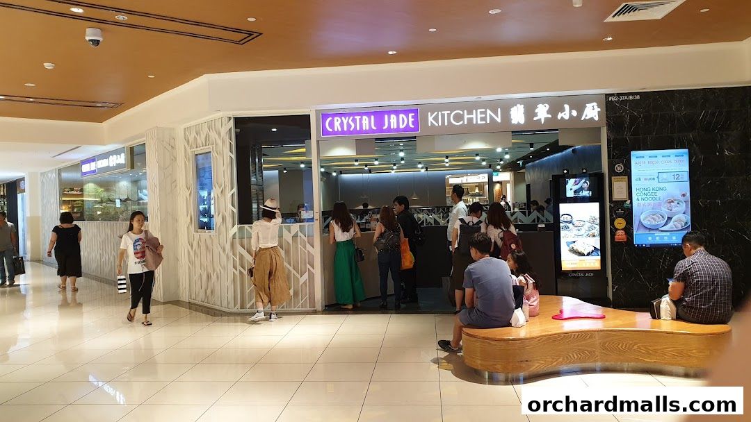 The entrance of Crystal Jade Kitchen restaurant with people queuing and digital displays.