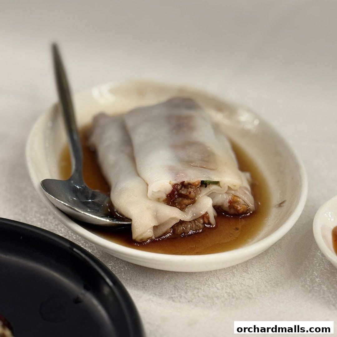 A close-up of a delicious dim sum dish, likely rice noodle rolls, served in a savory sauce.