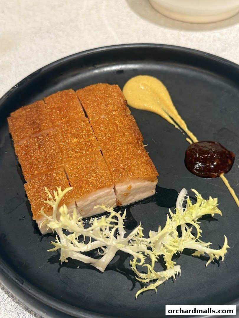 A plate of crispy roasted pork belly with dipping sauces and garnish.
