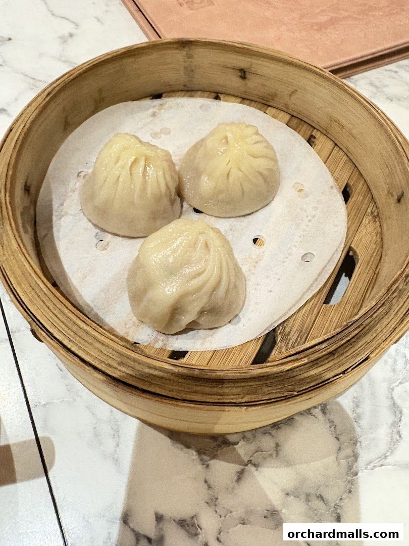 A bamboo steamer basket filled with three delicious soup dumplings on a marble table.