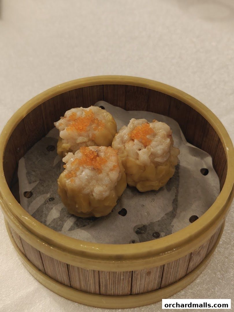 Three delicious dim sum dumplings in a bamboo steamer basket, topped with orange roe.
