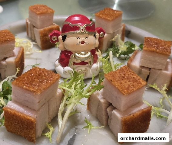 Crispy roasted pork belly cubes served with garnish and a decorative figurine.