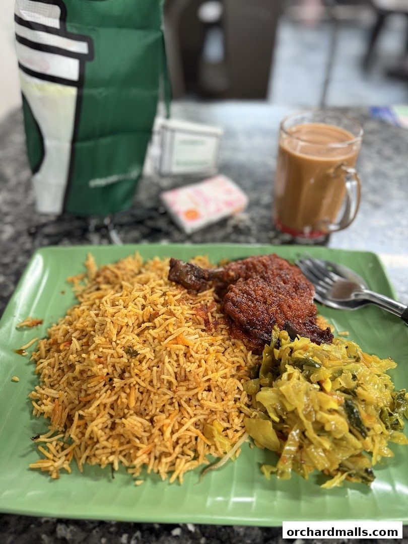A plate of biryani with chicken and vegetables, served with a cup of tea.