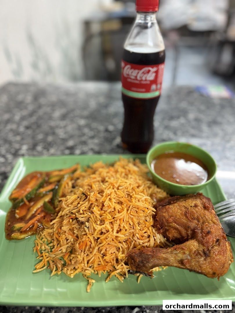 A plate of biryani with fried chicken and a side dish, served with Coca-Cola.