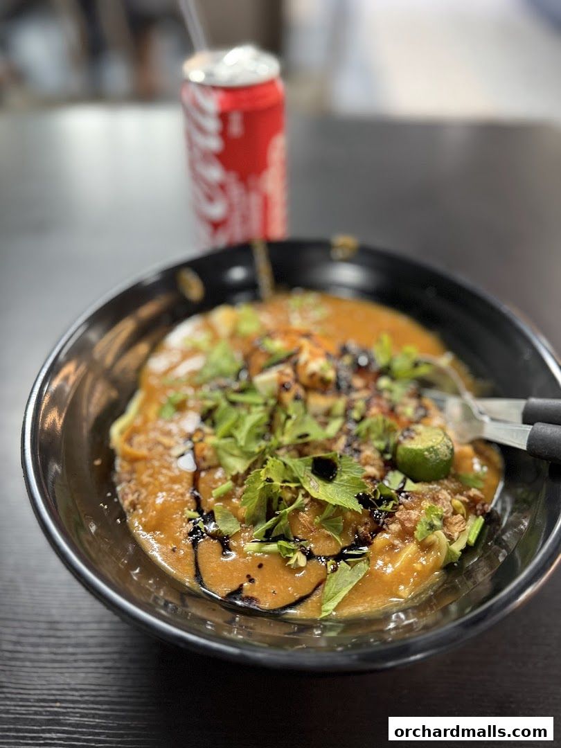 A close-up of a delicious bowl of curry noodles with a can of Coca-Cola in the background.