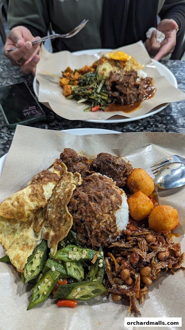Two plates of nasi lemak with various side dishes, served on brown paper.