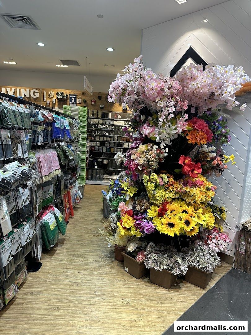 A wide aisle in a Daiso store, showcasing shelves of products and a vibrant display of artificial flowers.