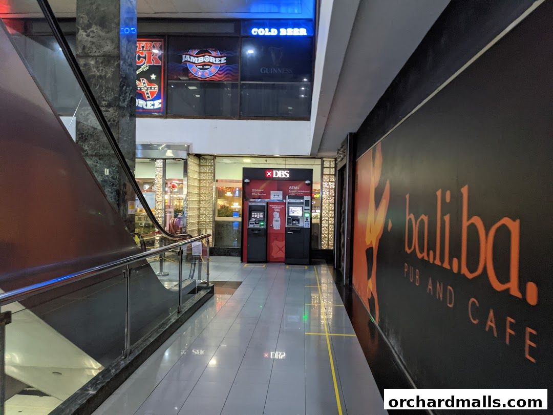 An interior view of a shopping mall corridor with an escalator and DBS ATMs.