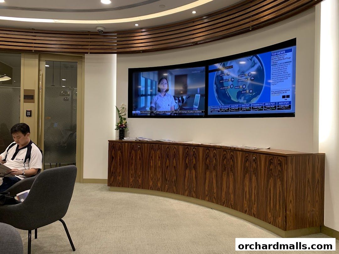 A man reads a newspaper in a waiting area with screens displaying news.