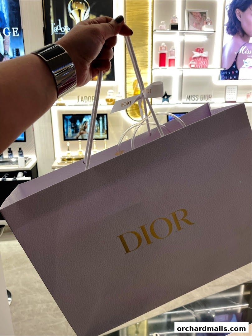 A hand holds a Dior shopping bag inside a beautifully lit Dior Beauty boutique.