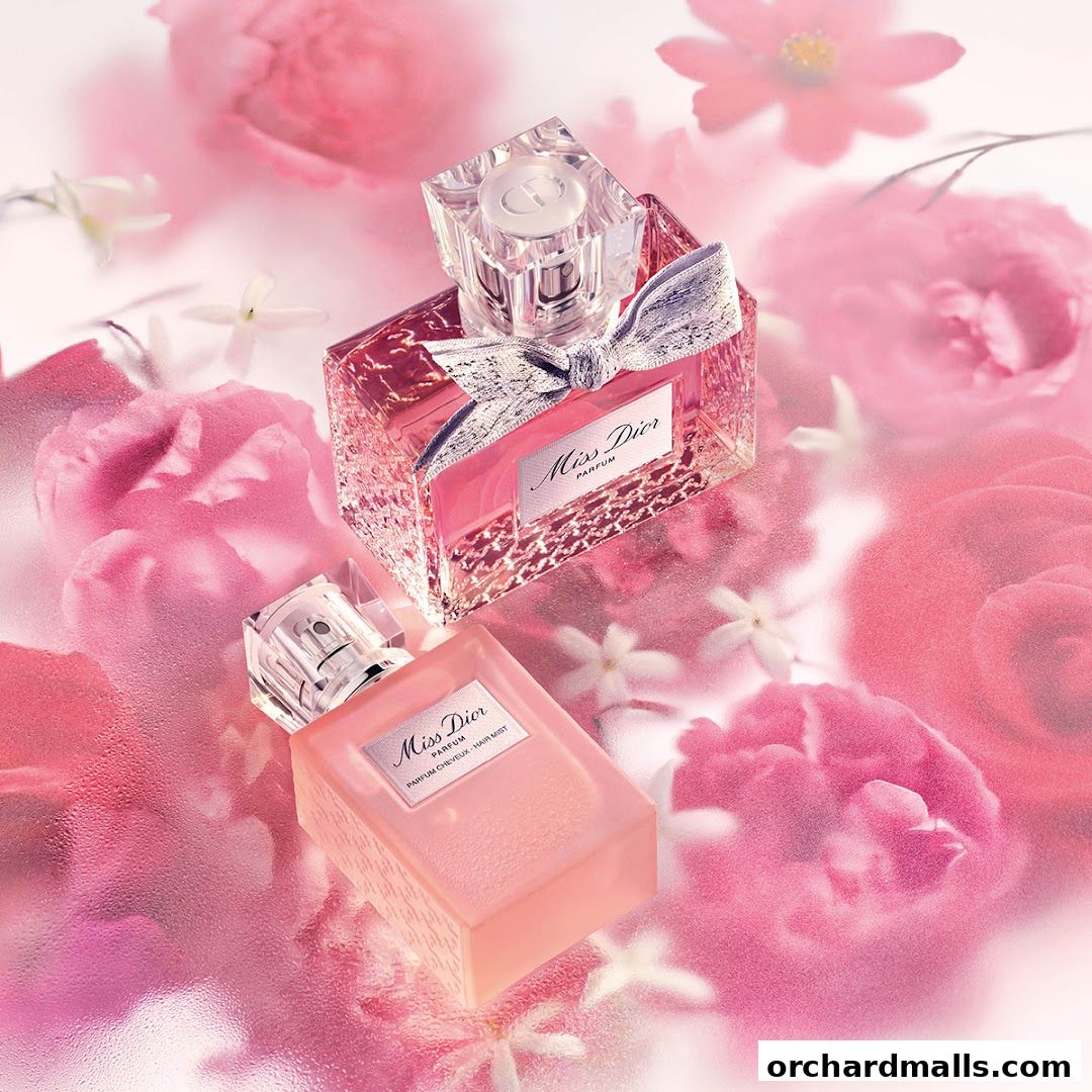 Two elegant bottles of Miss Dior perfume are displayed amidst a backdrop of soft pink roses and delicate white flowers.