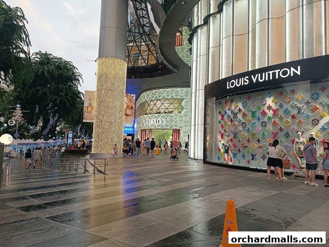 A street view of luxury brand stores, including Louis Vuitton and Prada, with people walking by.