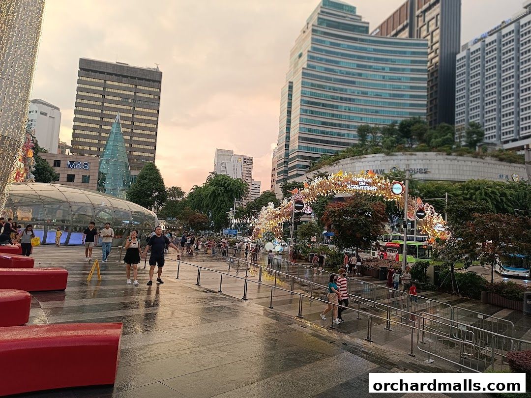 A bustling street scene with people walking, festive decorations, and modern buildings under a sunset sky.