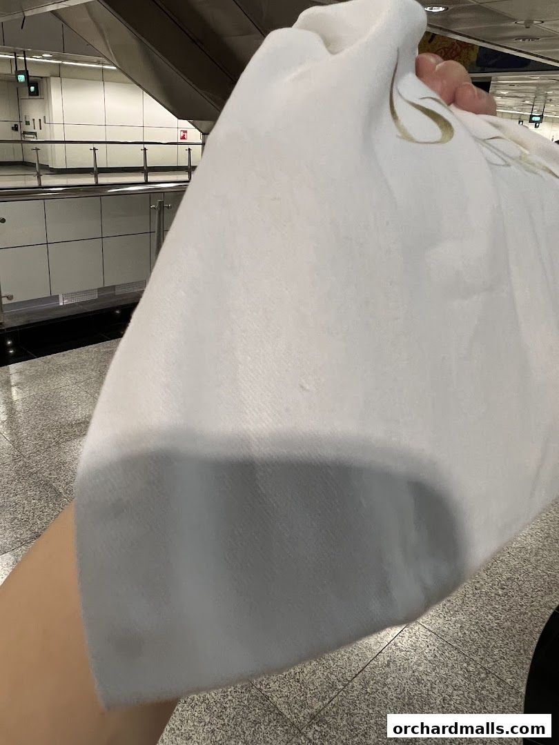 A hand holds a white Dior branded cloth in front of a blurred background.