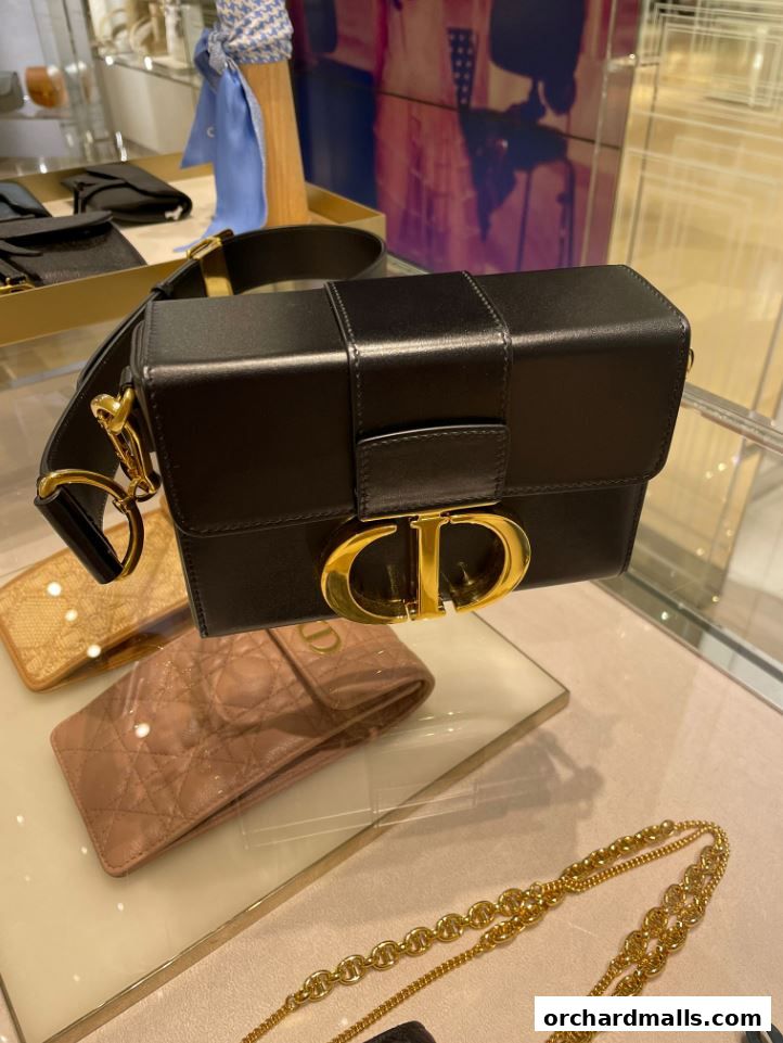 A black Dior handbag with gold CD logo displayed on a glass shelf.