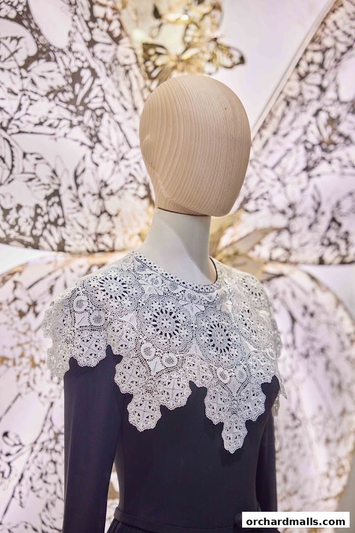 Mannequin displays a dark dress with an intricate white lace collar and a butterfly-themed backdrop.