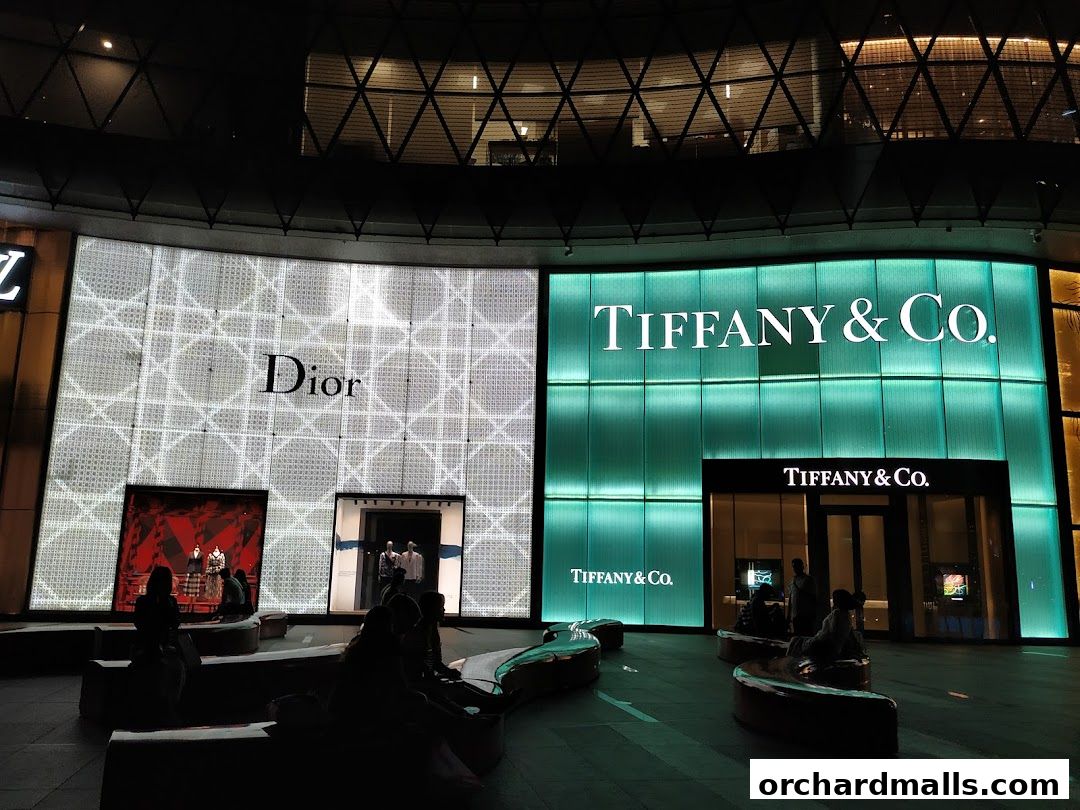 Dior and Tiffany & Co. storefronts illuminated at night with people sitting outside.